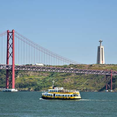 Ein Touristenboot überquert die Tejo-Mündung, im Hintergrund die Christusstatue.